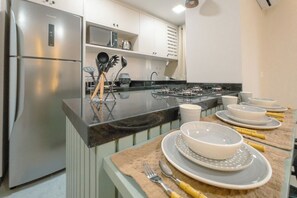 A modern kitchen with stainless steel appliances, a gas stove, and a dining area set with white plates and bowls. - Comfort and Convenience in Downtown Maringa - TV102 (Maringá)