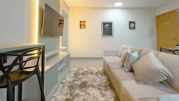 Ein modernes Wohnzimmer mit einer Couch, einem an der Wand befestigten Fernseher und einem Schreibtisch mit Stuhl.