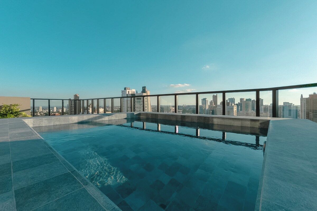 Une piscine à débordement située sur le toit, offrant une vue panoramique sur la ville et entourée d’une rambarde en verre.