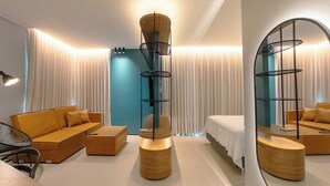 A modern hotel room with a sofa, a bed, a round wooden table, and a tall, cylindrical lamp. - Design and Modern Living in Downtown Maringa - NEO204 (Maringá)