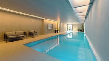 Piscina interna com superfície de água cristalina, teto com claraboias e área de estar com sofás e cadeiras.
