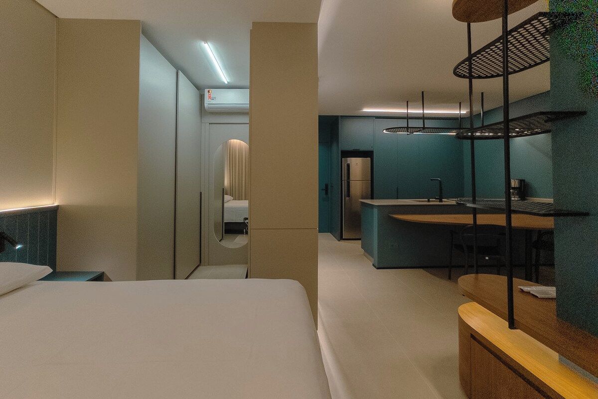 Quarto de hotel moderno com cama, escrivaninha e cozinha compacta.