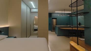 Quarto de hotel moderno com cama, escrivaninha e cozinha compacta.
