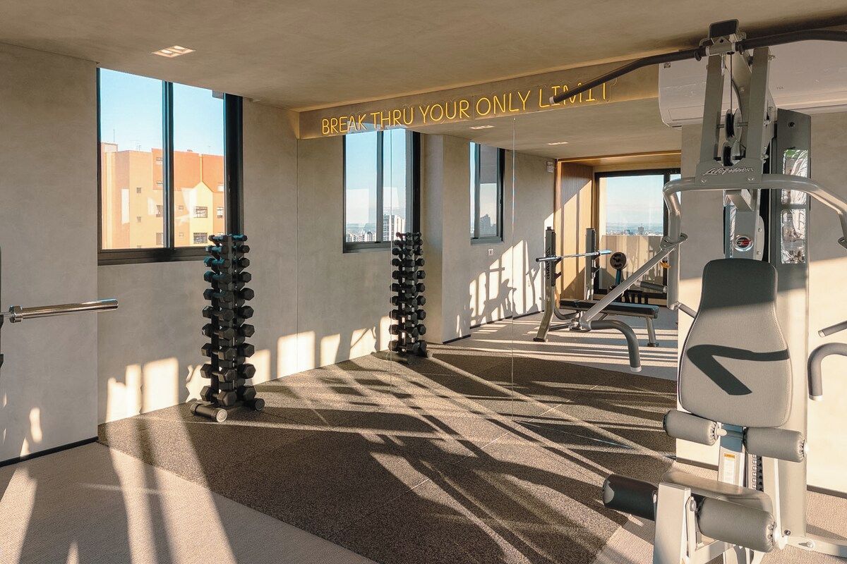 Uma academia com equipamentos de ginástica, um letreiro motivacional e grandes janelas.