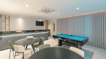 Espaço moderno com mesa de bilhar, área de estar e bar.