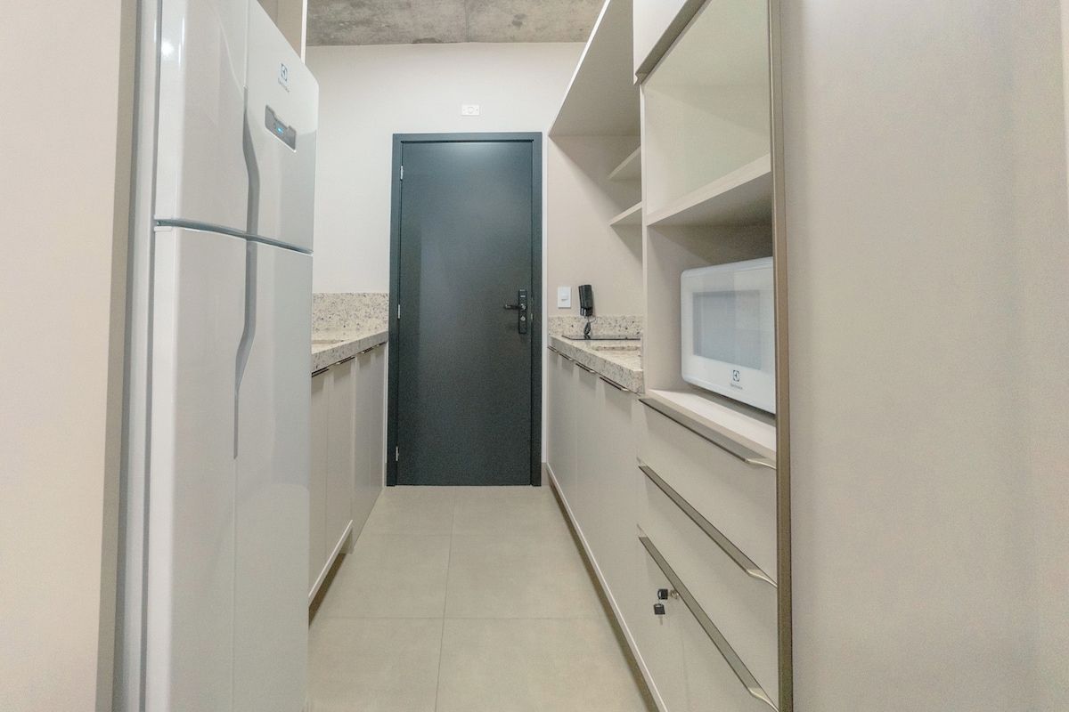 Cocina estrecha con refrigerador, microondas y una puerta al final.