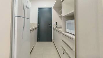 Cocina estrecha con refrigerador, microondas y una puerta al final.