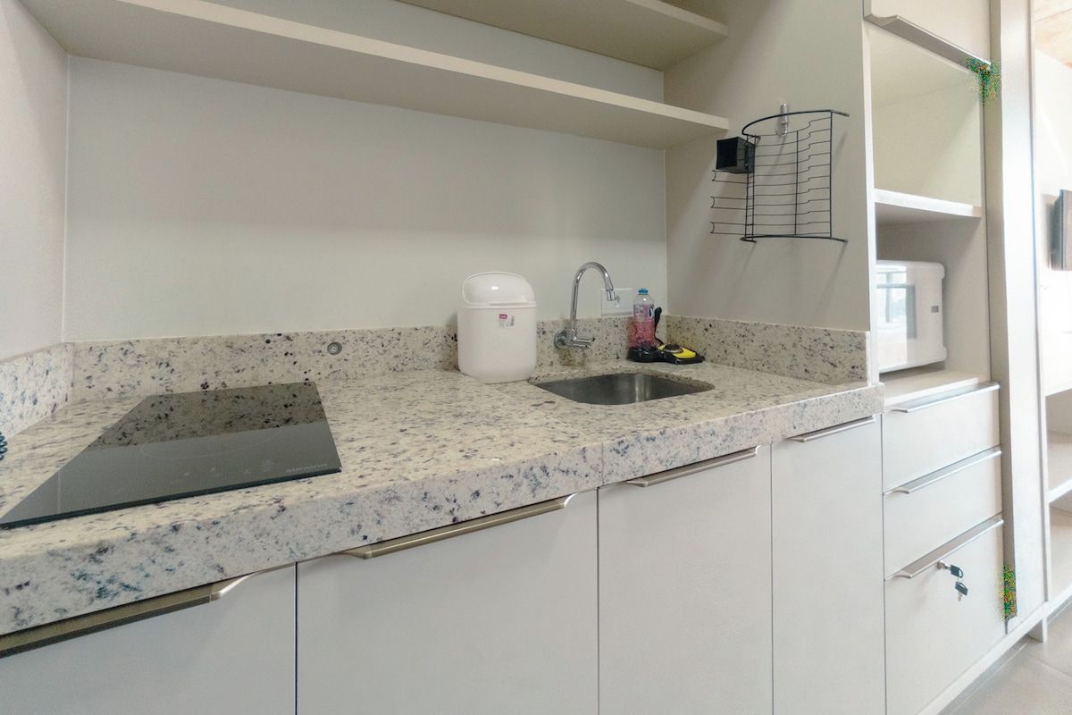 Una cocina con encimera de granito, un lavamanos de acero inoxidable, una cafetera blanca y una tabla de cortar negra.