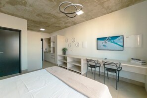 A modern bedroom with a bed, desk, chairs, and a painting on the wall.