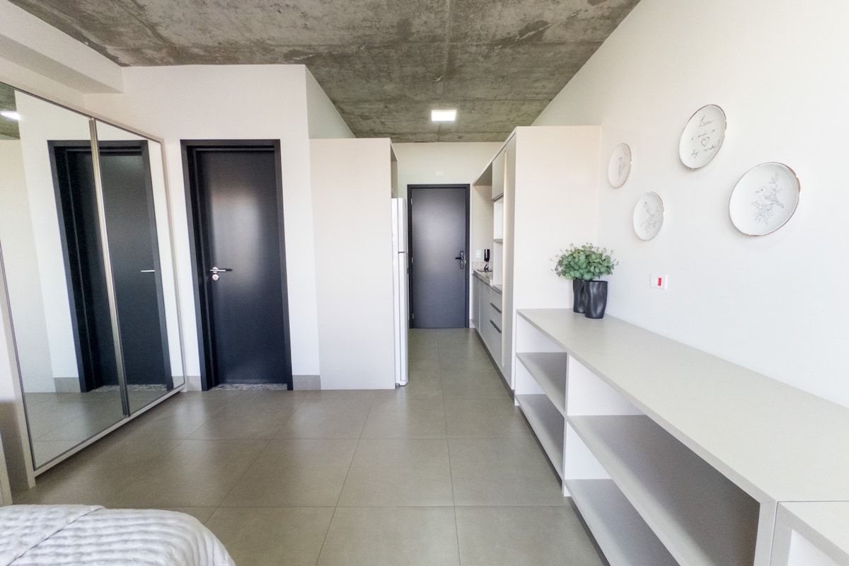 Interior moderno com um corredor que leva a um quarto, uma cama e um balcão com uma planta.