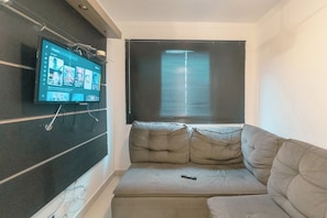 A living room with a flat-screen TV mounted on the wall, a sofa, and a window with blinds. - Spacious 3-Bedroom Family Apartment - AZ401-1 (Maringá)