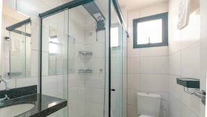 Kylpyhuoneessa on lasiseinällä varustettu suihku, valkoinen wc-istuin ja pesuallas, jonka yläpuolella on musta taso.