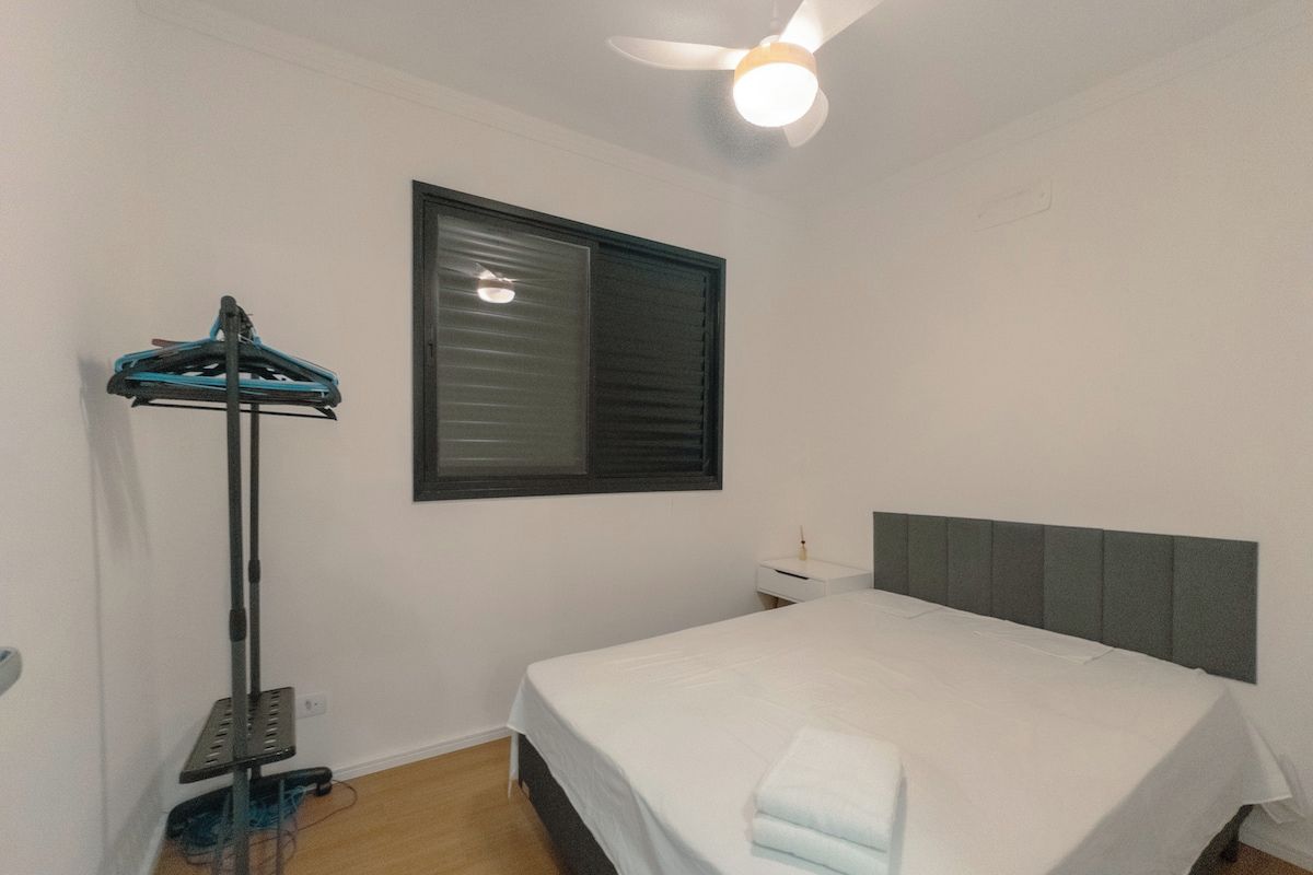 Ein Schlafzimmer mit einem Bett, einem Deckenventilator, einem Fenster mit Jalousien und einem kleinen Nachttisch.