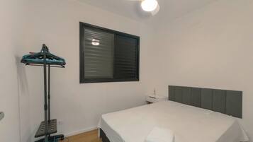 Ein Schlafzimmer mit einem Bett, einem Deckenventilator, einem Fenster mit Jalousien und einem kleinen Nachttisch.