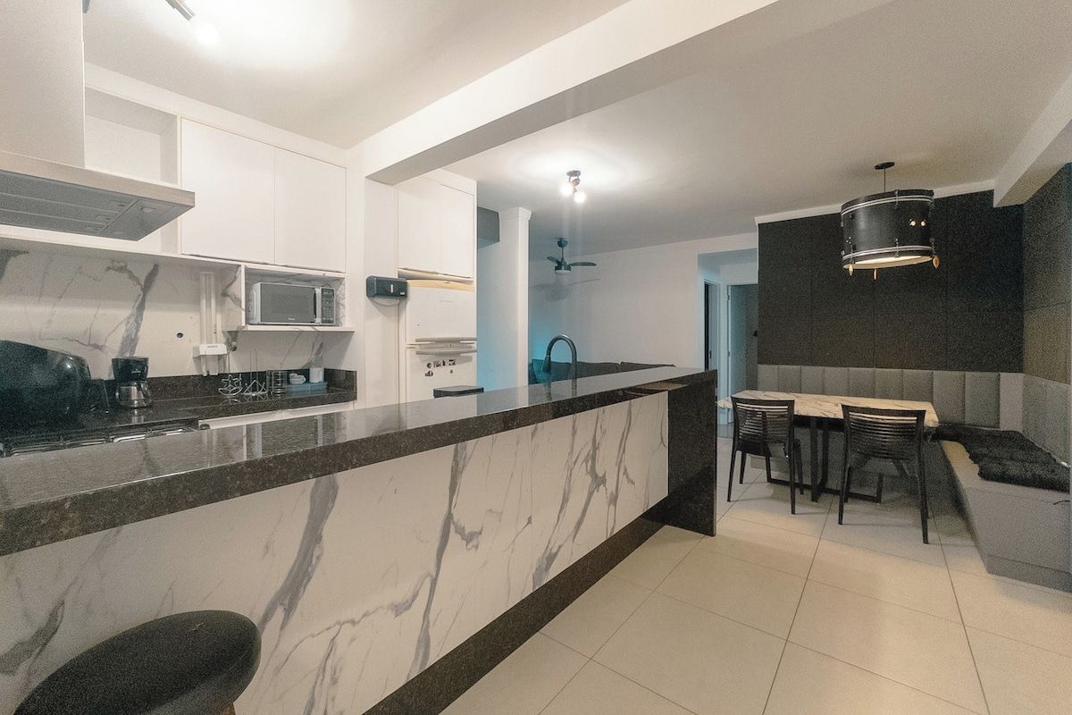 Una cocina moderna con encimera de mármol, microondas integrado y un comedor con mesa y sillas.