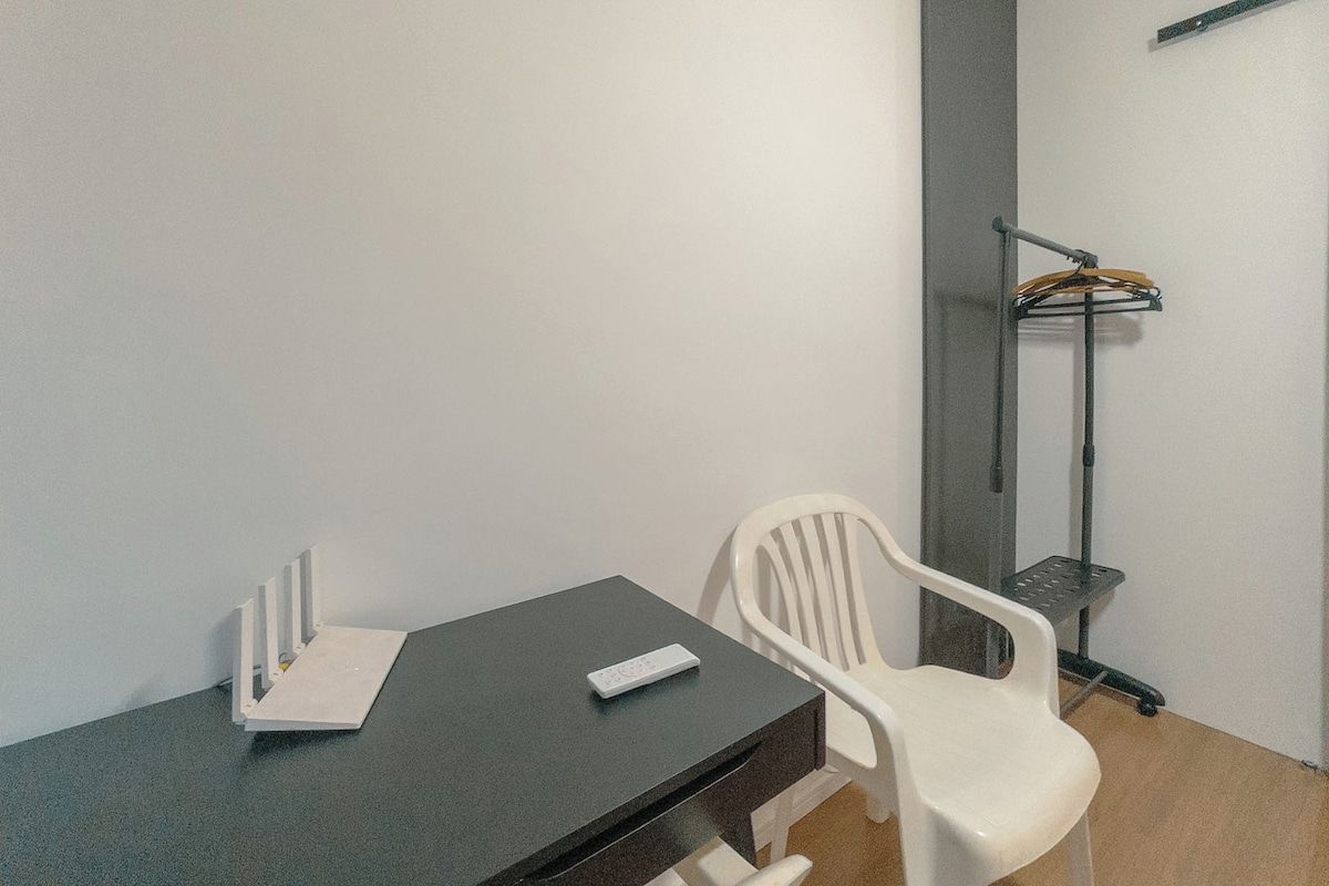 Una habitación con una mesa oscura, una silla blanca, una pizarra y una lámpara de pie.