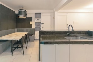 A modern kitchen with a marble countertop, a built-in sink, and a dining area with a table and chairs. - Spacious 3-Bedroom Family Apartment - AZ401-1 (Maringá)