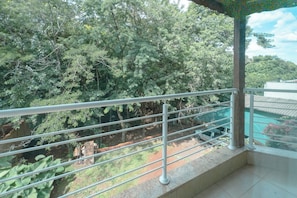 A balcony with a metal railing overlooking a garden area with trees and a swimming pool.