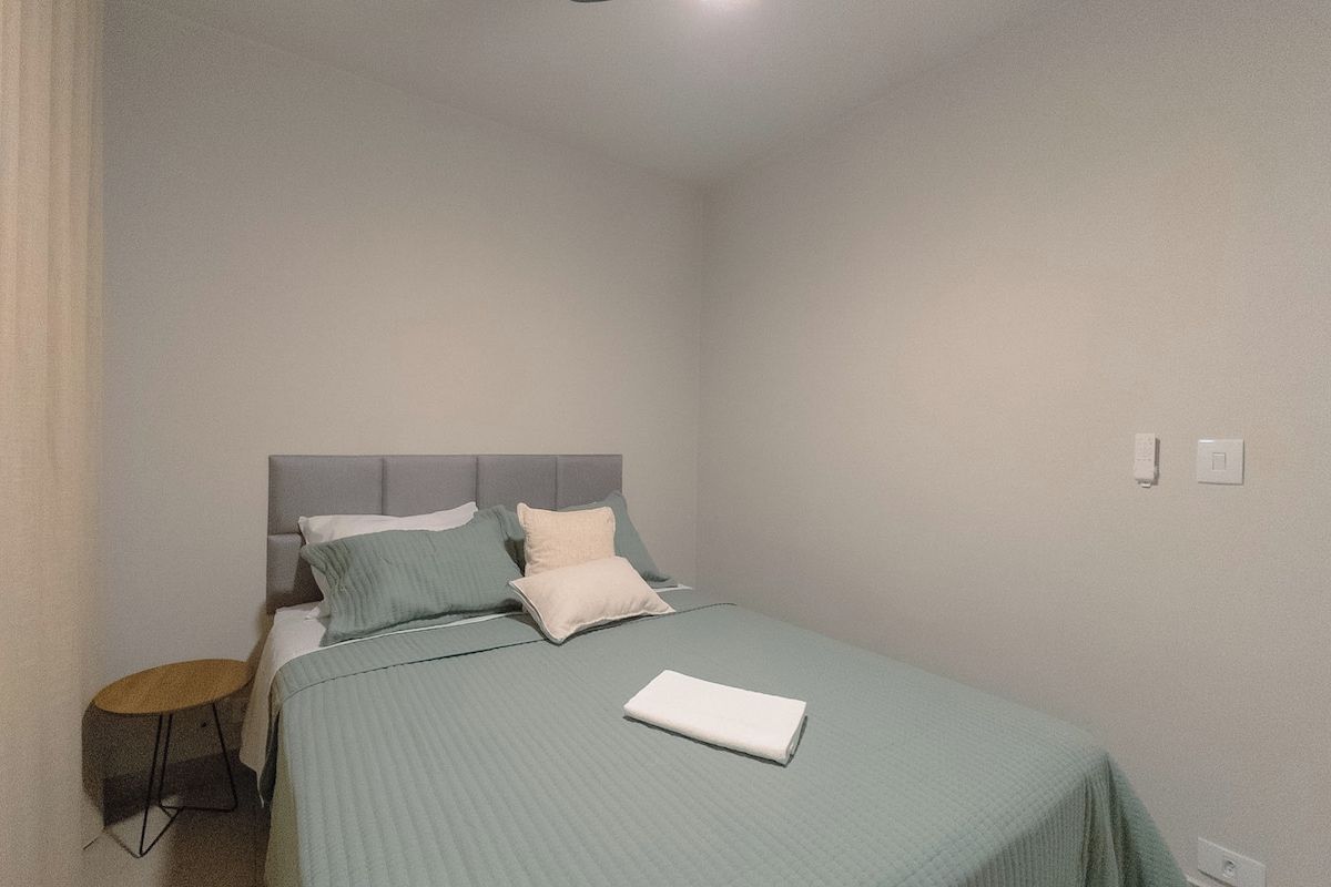 A bedroom with a bed, pillows, a bedside table, and a wall socket.