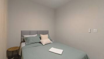 A bedroom with a bed, pillows, a bedside table, and a wall socket.