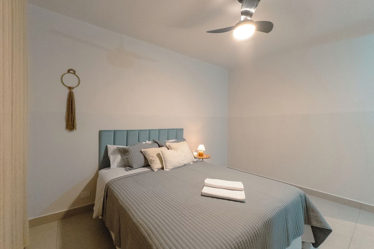 Une chambre à coucher comprenant un lit, une table de chevet, un ventilateur de plafond et un élément décoratif fixé au mur.