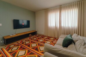 Un soggiorno con una TV a schermo piatto montata a parete, un divano e un tappeto decorato.