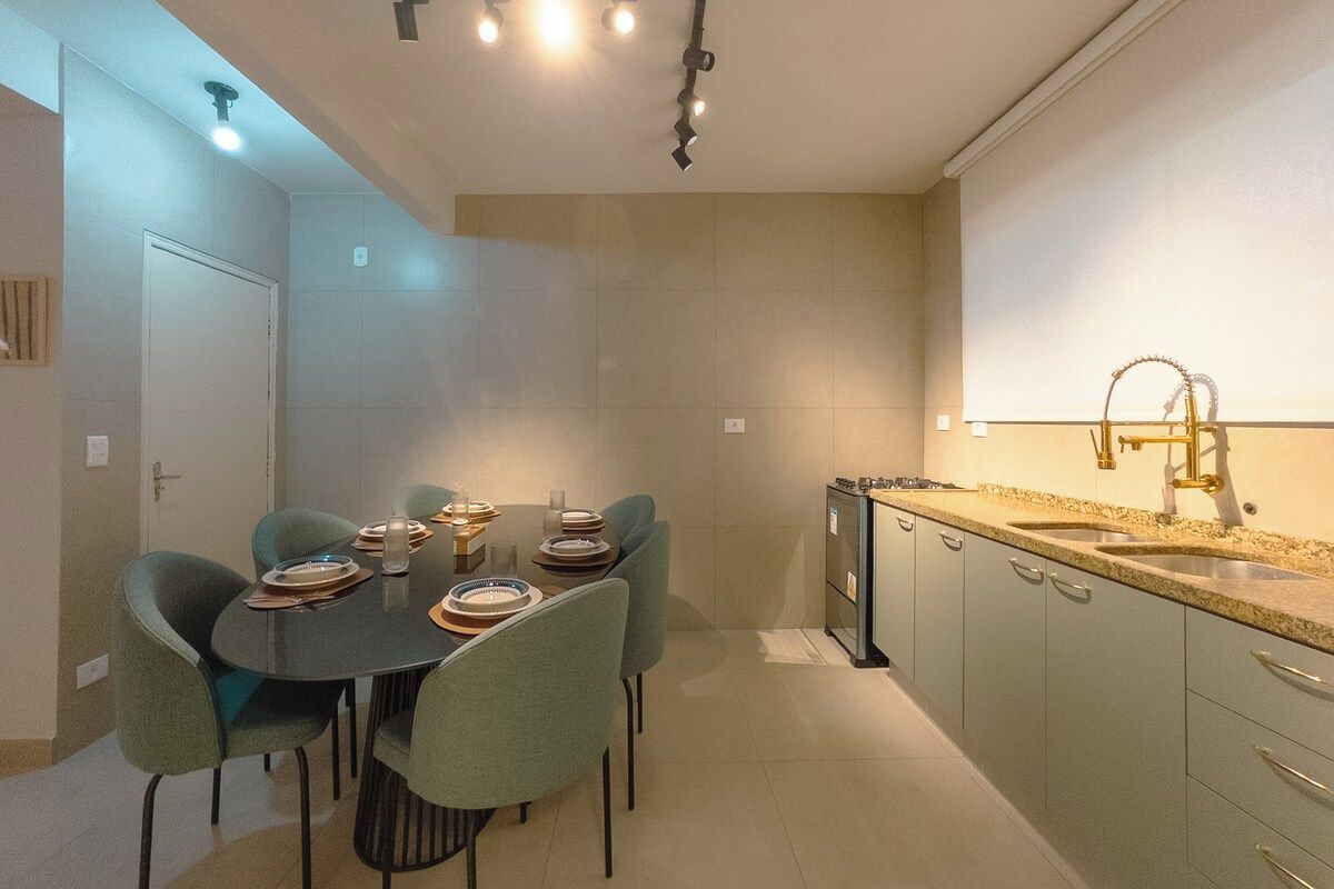 A modern kitchen with a dining area, featuring a round table with chairs, a built-in oven, and a sink with a gold faucet.