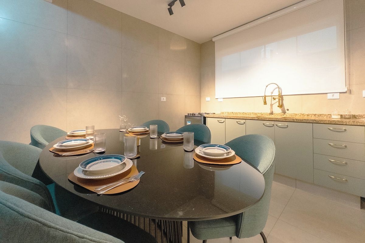 Un comedor moderno con una mesa redonda preparada para cuatro personas, rodeada de sillas color turquesa.