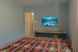 A bedroom with a bed, a television mounted on the wall, and a patterned rug.