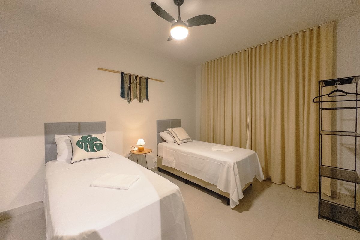 A hotel room with two beds, a ceiling fan, a lamp, and a window with curtains.
