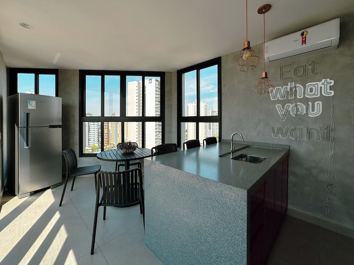 A modern kitchen with a central island, a built-in refrigerator, and a large window providing a view of high-rise buildings.