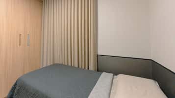 Een slaapkamer met een bed, een kledingkast en een raam met gordijnen.