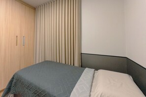 Un dormitorio con cama, armario y ventana con cortinas.