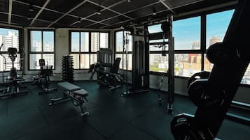 Een sportschool met diverse fitnessapparatuur, grote ramen en uitzicht op de stadsgezicht.