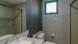 Ein modernes Badezimmer mit einem großen Spiegel, einem rechteckigen Waschbecken, einer Toilette und einer Duschkabine.