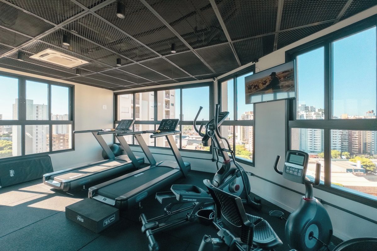 A gym with treadmills, an elliptical, and a stationary bike, large windows, and a city view.
