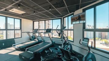 A gym with treadmills, an elliptical, and a stationary bike, large windows, and a city view.