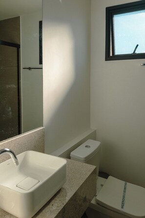 Een badkamer met een wit wastafel, een spiegel, een toilet en een raam.