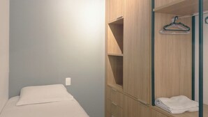Quarto com cama, guarda-roupa de madeira com várias prateleiras e um cabideiro.