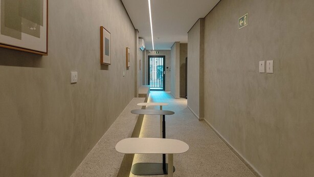 A hallway with a series of tables and chairs, a light fixture, and framed pictures on the walls.