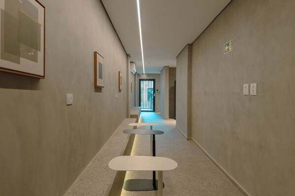 A hallway with a series of tables and chairs, a light fixture, and framed pictures on the walls.