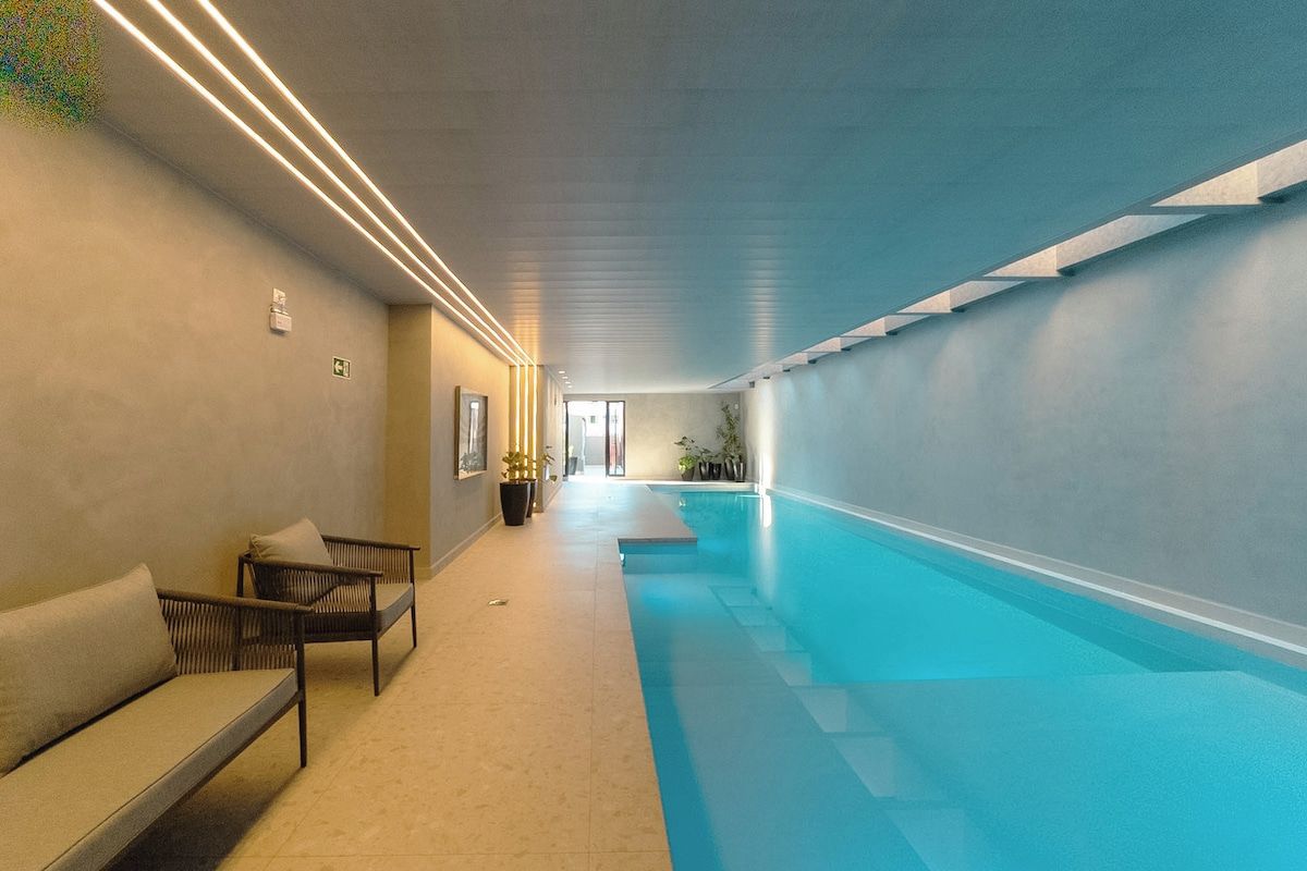 Ein moderner, überdachter Swimmingpool mit klarem, blauem Wasser, eine Lounge-Bereich mit Sofas und eine Treppe, die zu einer anderen Ebene führt.