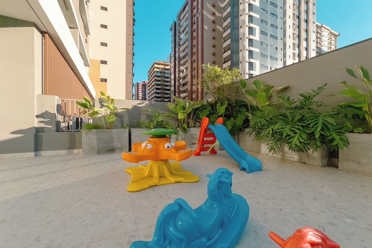 Espaço de recreação infantil com escorregadores e estruturas de escalada, cercado por edifícios residenciais altos.