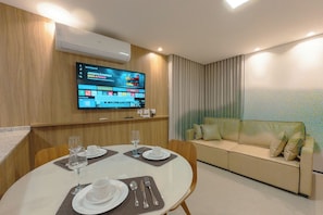 A hotel room with a dining table set for two, a television mounted on the wall, and a sofa. - Modern Downtown Apartment with Style - NEO1004 (Maringá)