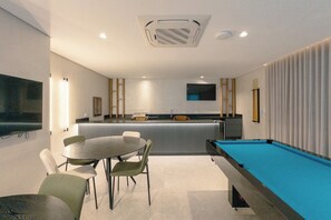 Een moderne kamer met een pooltafel, een eethoek met stoelen, een bar en een aan de muur bevestigde televisie.