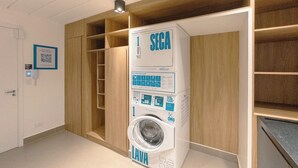 A compact, modern laundry room with a built-in washing machine, wooden shelving, and a QR code on the wall.