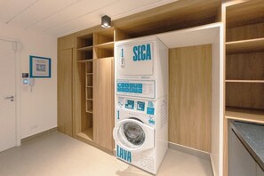 A compact, modern laundry room with a built-in washing machine, wooden shelving, and a QR code on the wall.