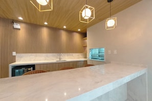 A modern kitchen with a marble countertop, wooden paneling, and pendant lighting. - Modern Downtown Apartment with Style - NEO1004 (Maringá)