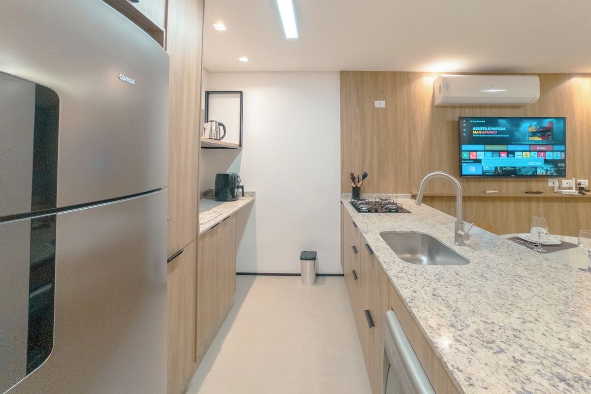 Cozinha moderna com geladeira de aço inoxidável, bancada de granito e televisão de tela plana fixada na parede.