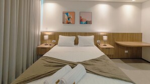 A hotel room with a large bed, two bedside tables, a wooden headboard, and two wall-mounted artworks.